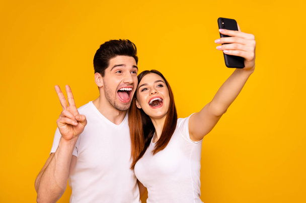Portrait of his he her she two nice attractive lovely stylish trendy cheerful positive people making taking selfie enjoying showing v-sign isolated over vivid shine bright yellow background - Photo, image