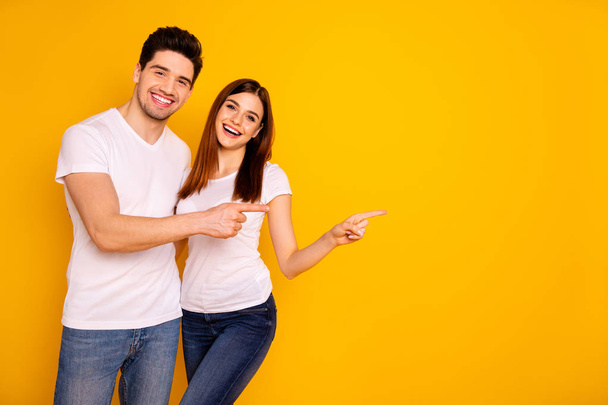 Close up photo beautiful she her he him his pair wondered direct indicate fingers empty space sale discount great little low price wear casual jeans denim white t-shirts isolated yellow background - Φωτογραφία, εικόνα
