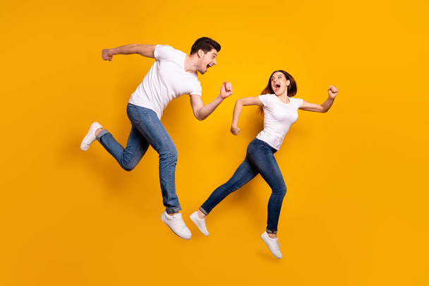 Full length side profile body size photo funky she her he him his pair jumping high hurry shopping raised fists yell scream shout loud wear casual jeans denim white t-shirts isolated yellow background - Foto, afbeelding