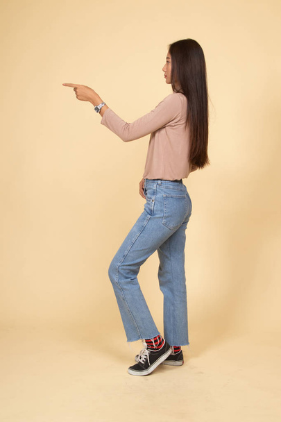 Full body side view of beautiful young asian woman pointing. - Foto, imagen