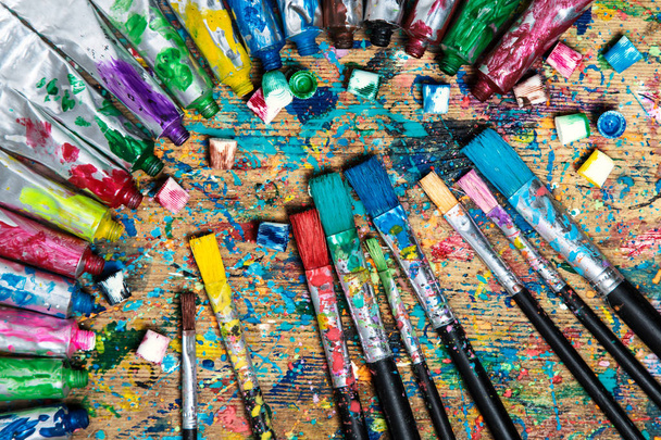 Vista superior. Antigua mesa de artista manchada con tubos de pintura acrílica y pinceles. Formación artística
 - Foto, Imagen
