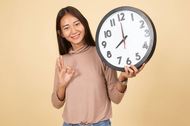 Young Asian woman show OK with a clock. - Zdjęcie, obraz