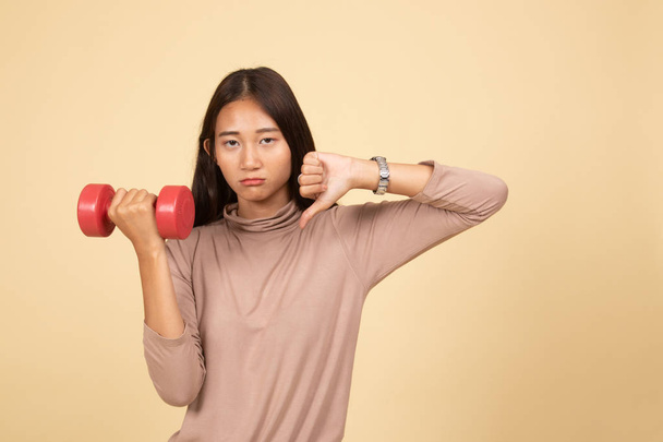 Unhappy Asian woman thumbs down with dumbbells. - Foto, afbeelding