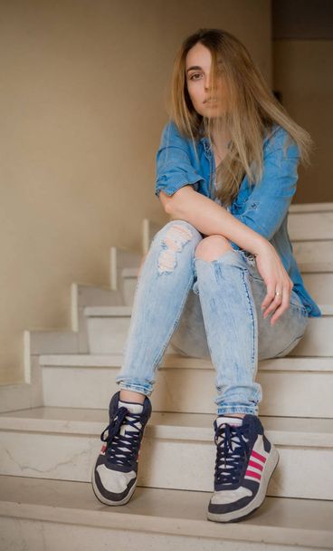young stylish woman posing sitting on stairs and looking at camera - Фото, зображення