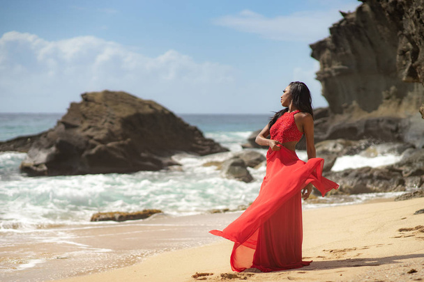 Kaunis aistillinen nainen yllään ylellinen punainen mekko ja poseeraa vieressä hiekkakallioita
 - Valokuva, kuva