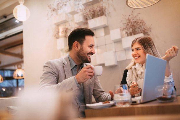Two beautiful young smiling businesspeople sitting at cafe, talking and drinking coffee. - Foto, Imagen