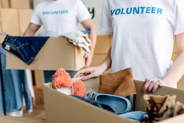 partial view of volunteers unpacking cardboard boxes with clothes and footwear - 写真・画像