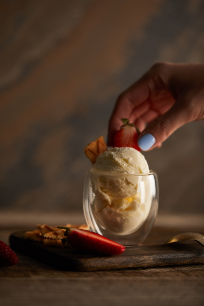 ガラスのアイスクリームにイチゴを置く女性のトリミングビュー - 写真・画像