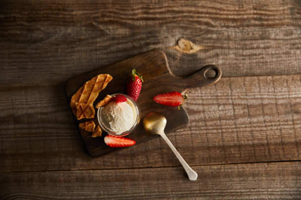 top view of ice cream in glass with strawberries and pieces of waffle on cutting board on table with copy space - Photo, image