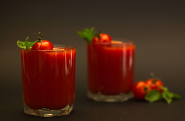 Two glasses of tomato juice with cherry tomatoes and mint with a black background - Fotoğraf, Görsel