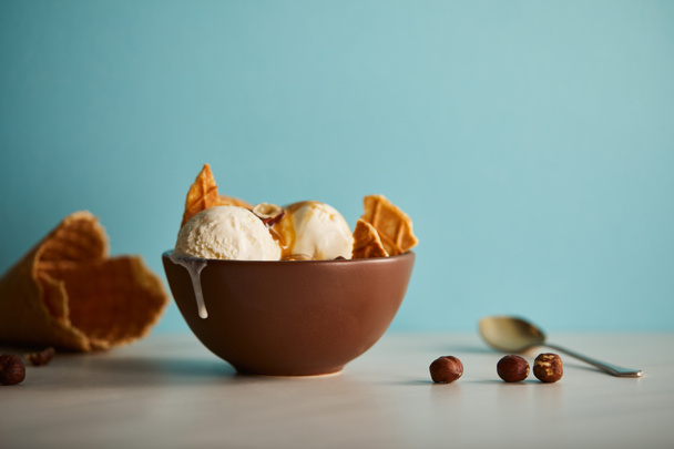 bowl of delicious ice cream with pieces of waffle and hazelnuts on blue - Foto, imagen