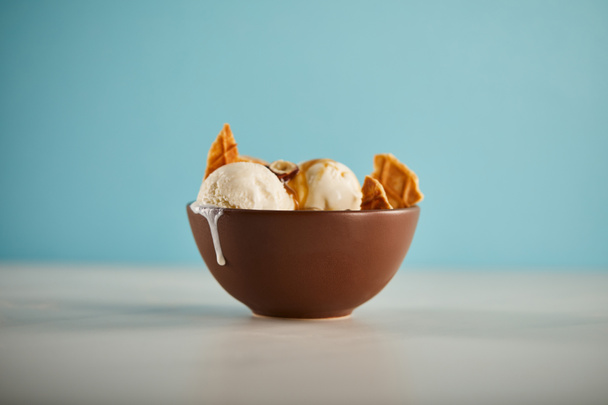 selective focus of bowl with delicious melting ice cream scoops and pieces of waffle on blue  - Фото, зображення