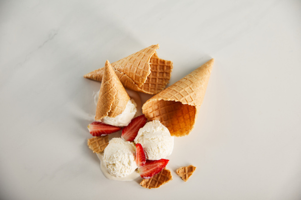 top view of cones and delicious melting ice cream with strawberries on grey surface - Fotografie, Obrázek