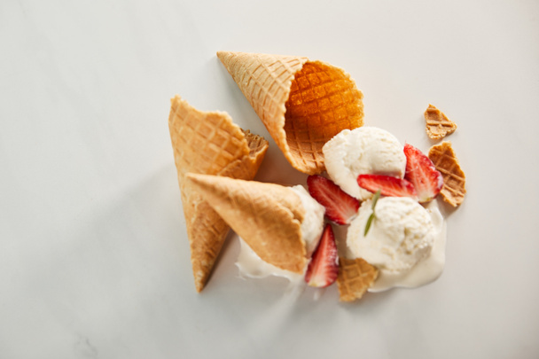 top view of cones and delicious melting ice cream with strawberries on grey - Fotografie, Obrázek