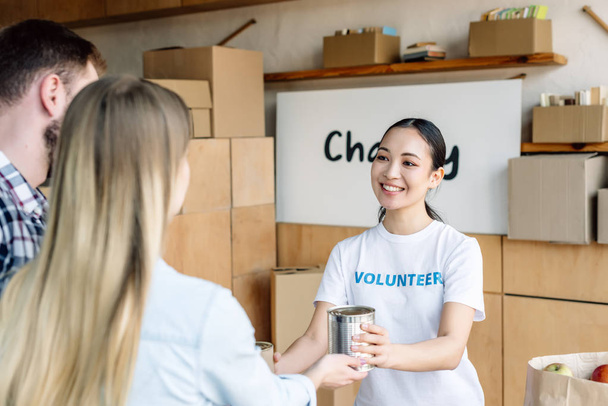 jolie asiatique bénévole donnant de la nourriture en conserve à l'homme et la femme dans la charité centre
 - Photo, image