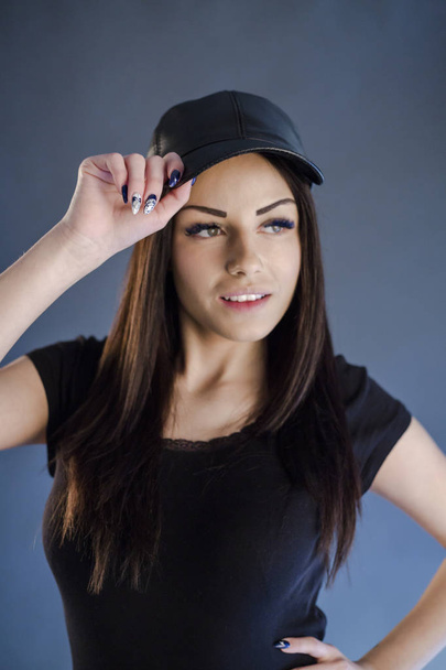 brunette girl holding her cap while posing in studio - Photo, Image