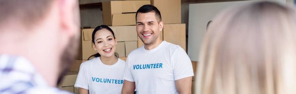 panoramic shot of smiling multicultural volunteers meeting people in charity center - Фото, зображення