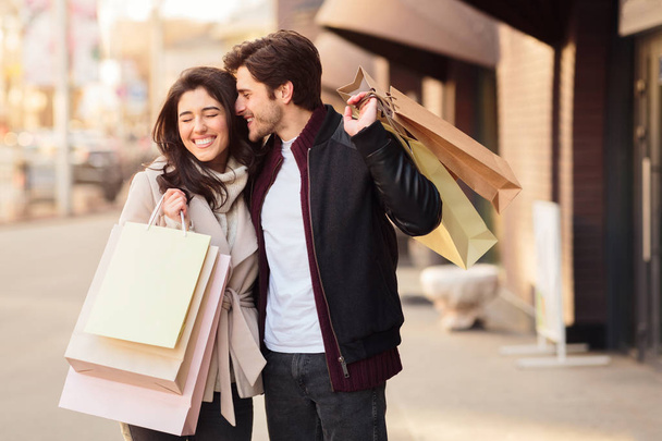 Kaufen kann man es nicht. glückliches Paar mit Einkaufstüten, Mann flüstert Frau zu - Foto, Bild