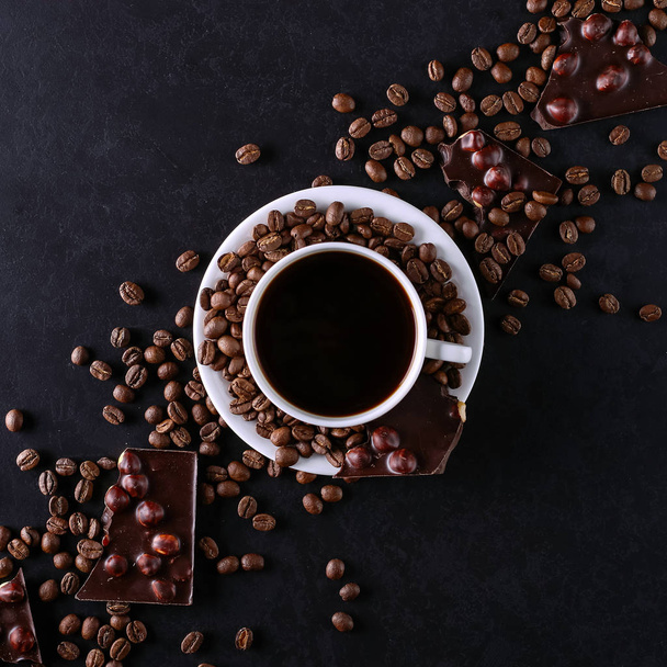 Scattered coffee grains, a cup and black chocolate on a black stone table. Copy space. - Fotoğraf, Görsel