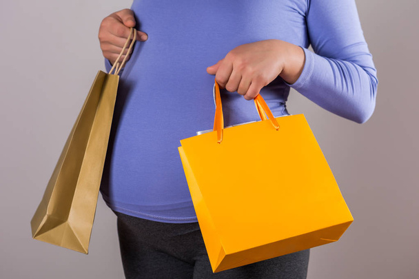 Image of pregnant woman holding shopping bags on gray background. - Foto, Imagem
