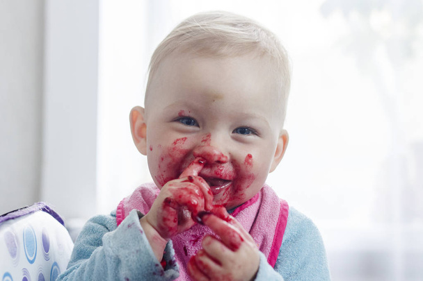 Een klein kind eet verse bessen en smeerde zijn gezicht. Zeer grappig beeld. - Foto, afbeelding