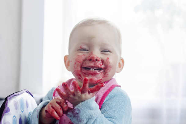 Małe dziecko zjada świeże jagody i rozmazane twarz. Bardzo śmieszne zdjęcia. - Zdjęcie, obraz