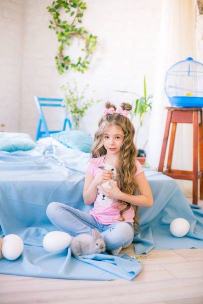 Little cute girl with long curly hair on the bed with little bunnies and Easter decor at home. - Foto, afbeelding