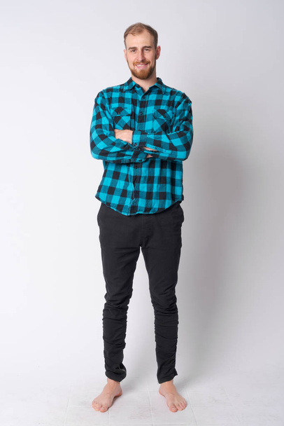 Full body shot of happy young bearded hipster man smiling with arms crossed - Fotó, kép