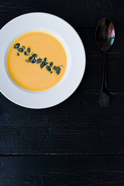 Тыквенный суп с семенами в белой тарелке на черном фоне
. - Фото, изображение