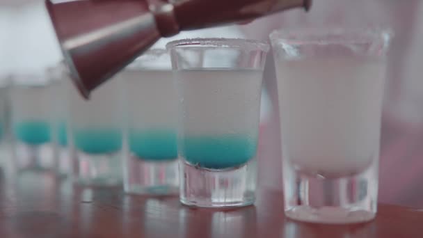 Closeup of barman's hand pouring blue Curacao liqueur into shot glass. Row of blue tropical shots cocktails at the bar - Footage, Video