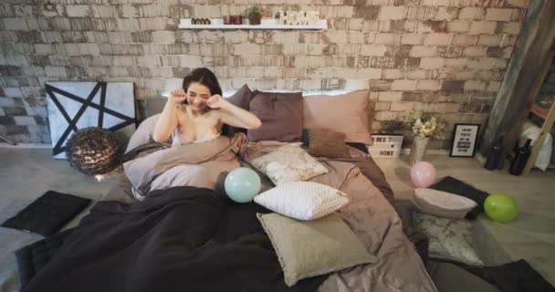 In modern loft bedroom charismatic lady waking up in the morning after a birthday party she stretching body with smile looking around , colorful balloons around - Filmagem, Vídeo