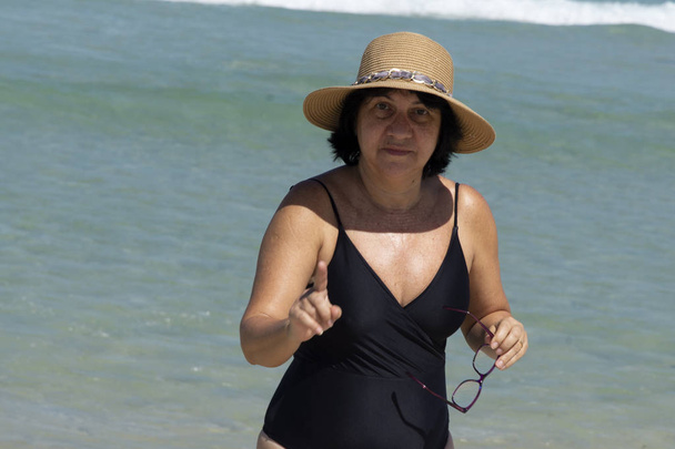 Mulher de meia-idade usando chapéu na praia e no mar como fundo
 - Foto, Imagem
