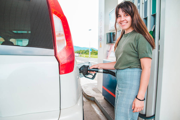 ガソリンスタンドの若い可愛い女性が車のタンクを満たし - 写真・画像