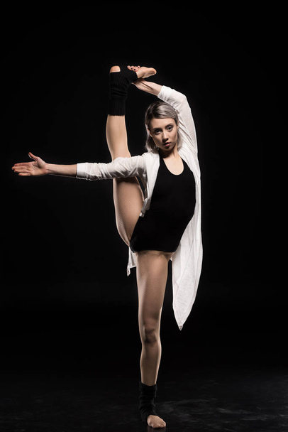 woman in bodysuit stretching before dancing on black - Valokuva, kuva