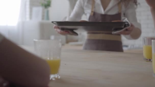 Hands of unrecognizable mother puts fresh baked pies on the table, her hungry sons take bakery. Big friendly noizy family having breakfast with sweets and orange juice together - Video, Çekim