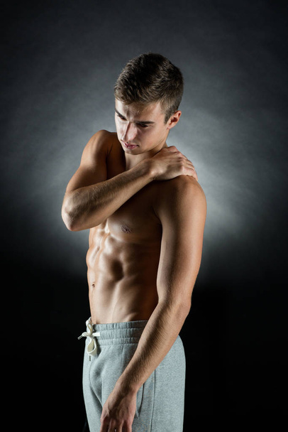 pain relief, sport, bodybuilding, health and people concept - young man standing over black background - Foto, afbeelding
