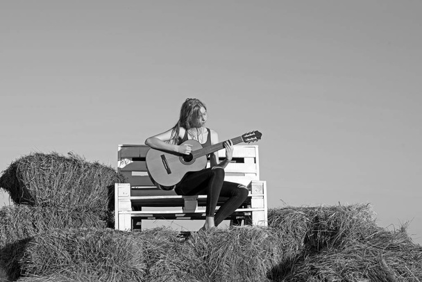 Woman play guitar on wooden bench. Woman guitarist hold acoustic guitar on sunny nature - Fotografie, Obrázek