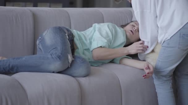 The young mother fall asleep at home. Teen son puts pillow under woman head and then lies near mom on the sofa. Woman is tired, she had difficult day. Caring for parents - Séquence, vidéo