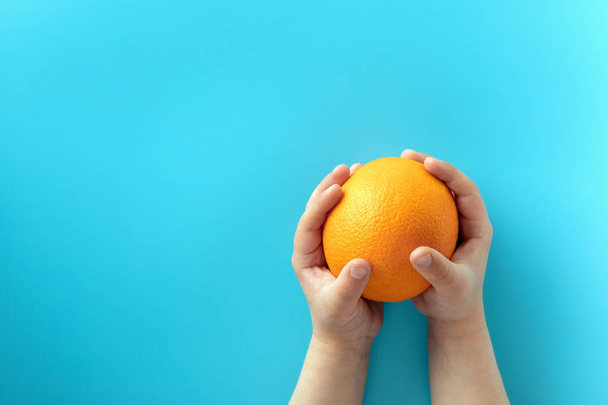 Orange on the blue background in the hands of a child. Healthy eating concept - Foto, immagini