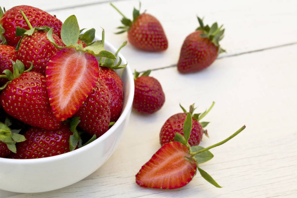 Fresh strawberries in ceramic bowl on white wooden background. - Photo, Image