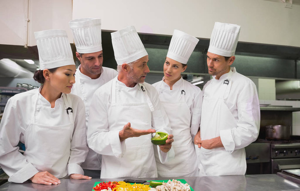 Row of trainee chefs slicing vegetables with tutor watching in a commercial kitchen - 写真・画像