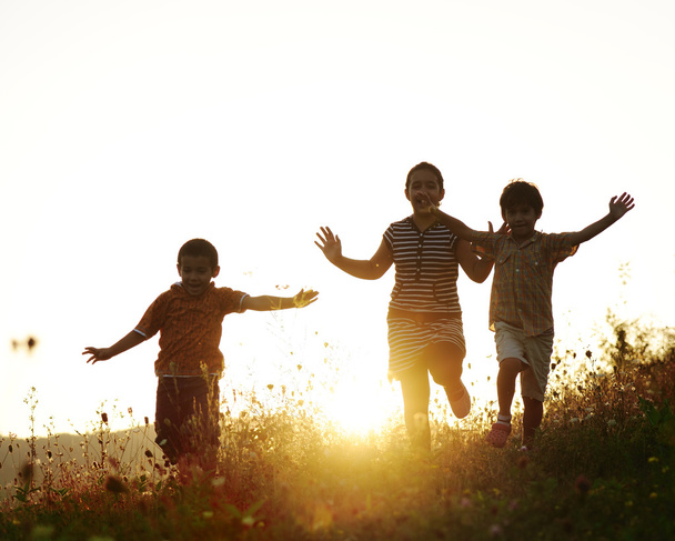 Children running on meadow at sunset - Фото, изображение