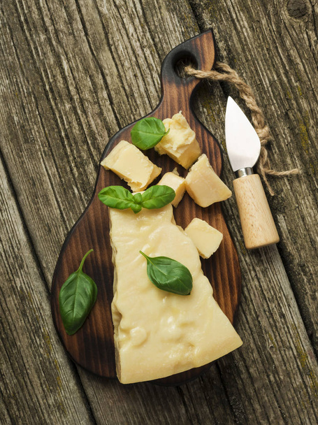 Piece of parmesan cheese with basil leaves and cheese knife on a wooden board. Top view - Valokuva, kuva