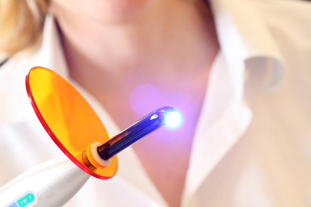 Dentist holds a lit dental curing UV light - Фото, изображение