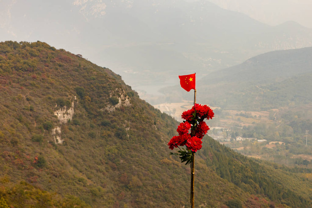China vlag en rode bloemen op een paal in de bergen - Foto, afbeelding