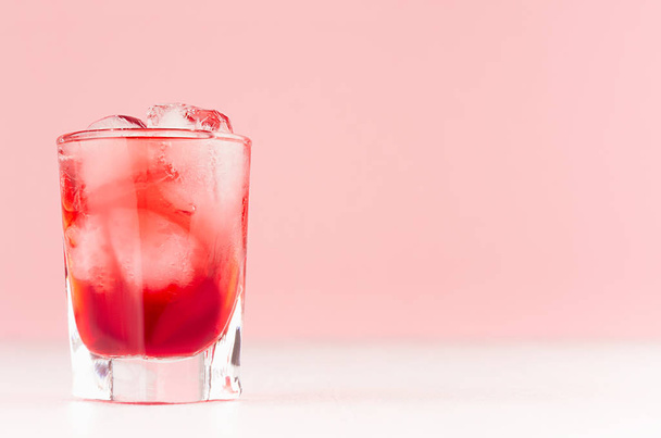 Exquisite cold red alcoholic liquor with ice cubes in shot glass closeup on white wood table and pastel pink wall, copy space. - Foto, Imagem