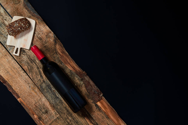 De arriba disposición de la botella de vino y pan de grano entero en tablones de madera
 - Foto, imagen