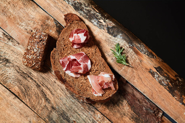 Arranged black bread slices with prosciutto slices and grapes on wooden planks from above. - Photo, image