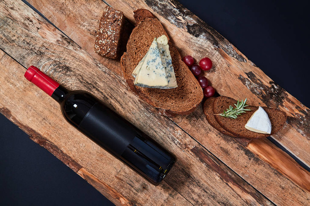 Top view of composed bread slices with blue cheese and grapes on wooden planks with bottle of wine - Фото, зображення