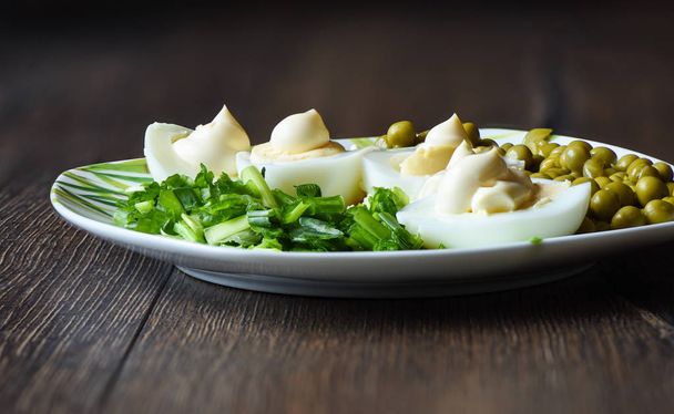 Boiled eggs under mayonnaise with green peas and green onions. A traditional russian dish. - Foto, imagen